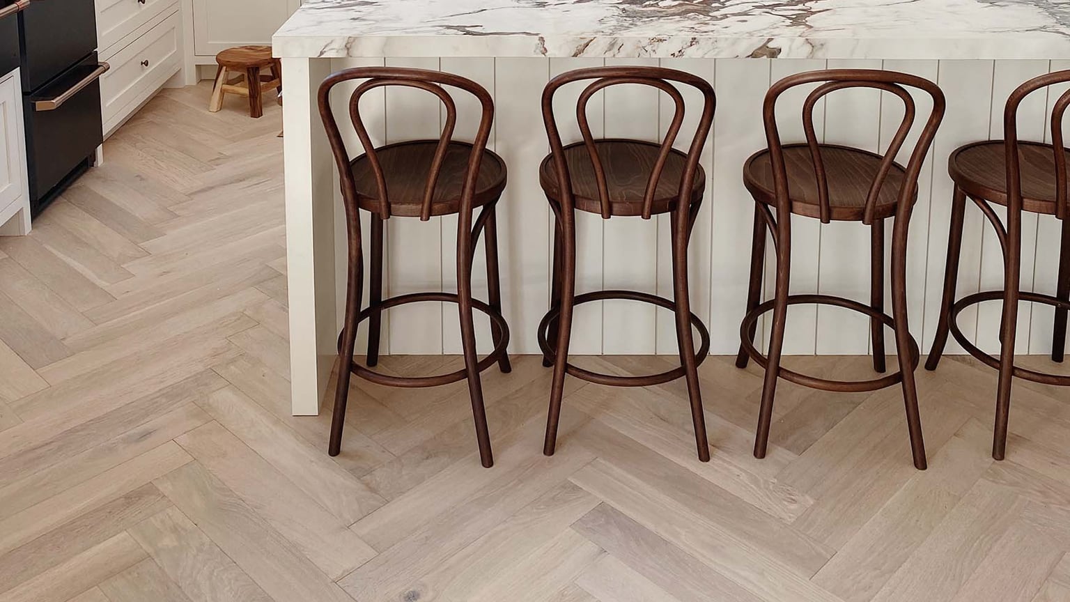 Pale oak herringbone floor in a kitchen with a marble island and bentwood stools