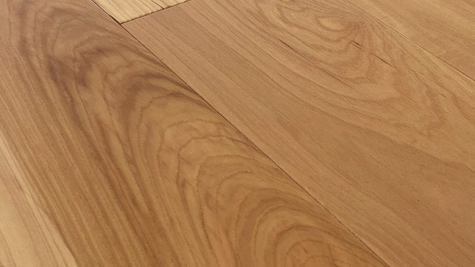 A close angled photograph of golden hickory floorboards meeting at a diagonal joint, their grain and soft sheen filling the frame.