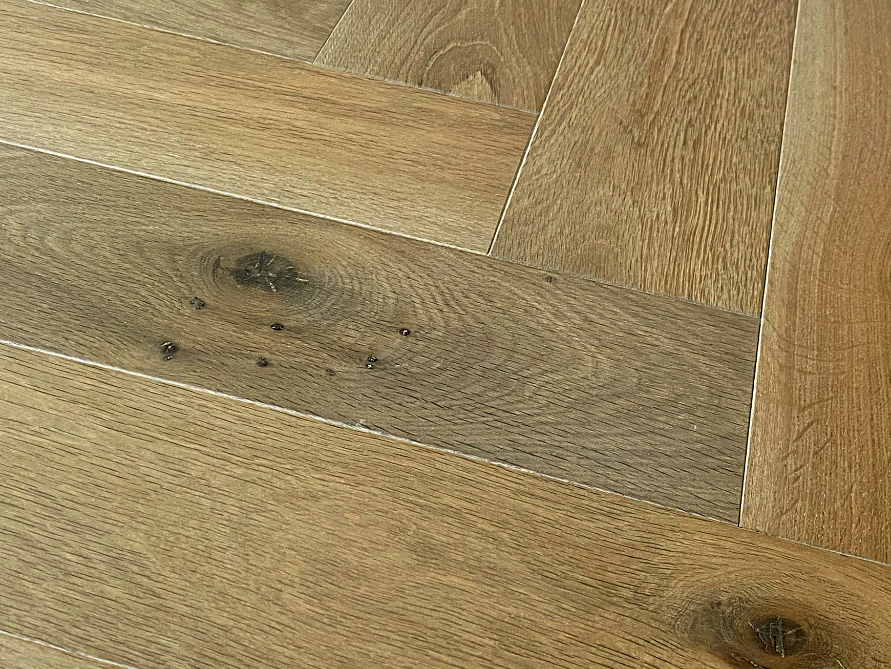 Close-up of warm brown oak herringbone with a large knot, dark filled pinholes and bevelled joints