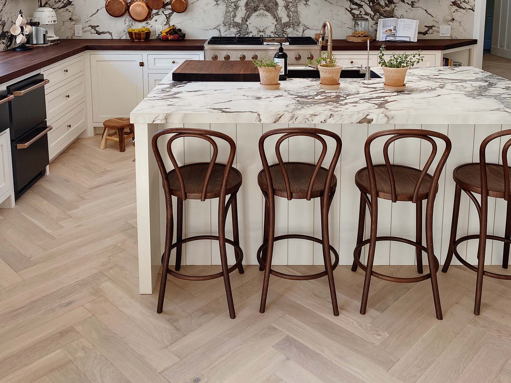 Pale oak herringbone floor in a kitchen with a marble island and bentwood stools