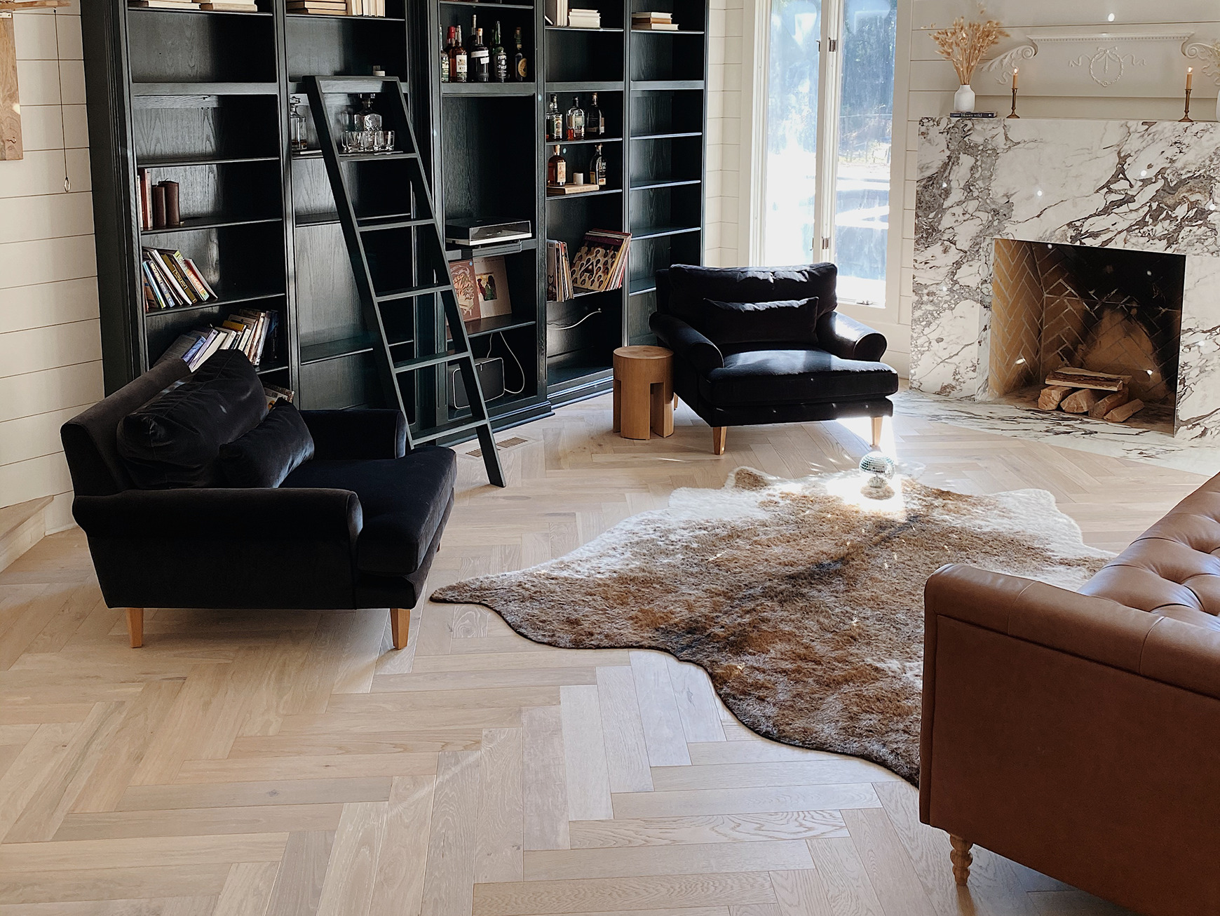 Pale oak herringbone floor in a living room with a black bookcase and a marble fireplace