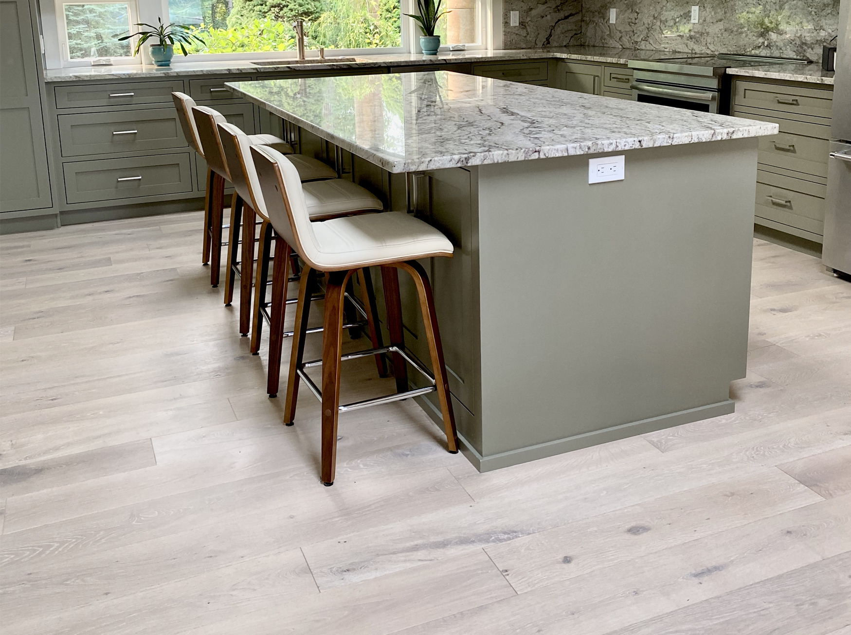Pale oak planks in a kitchen with a green island and walnut stools