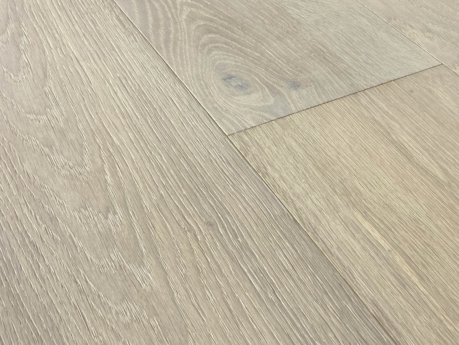Low-angle close-up of grey-beige oak planks with crisp wire-brushed texture and an end joint