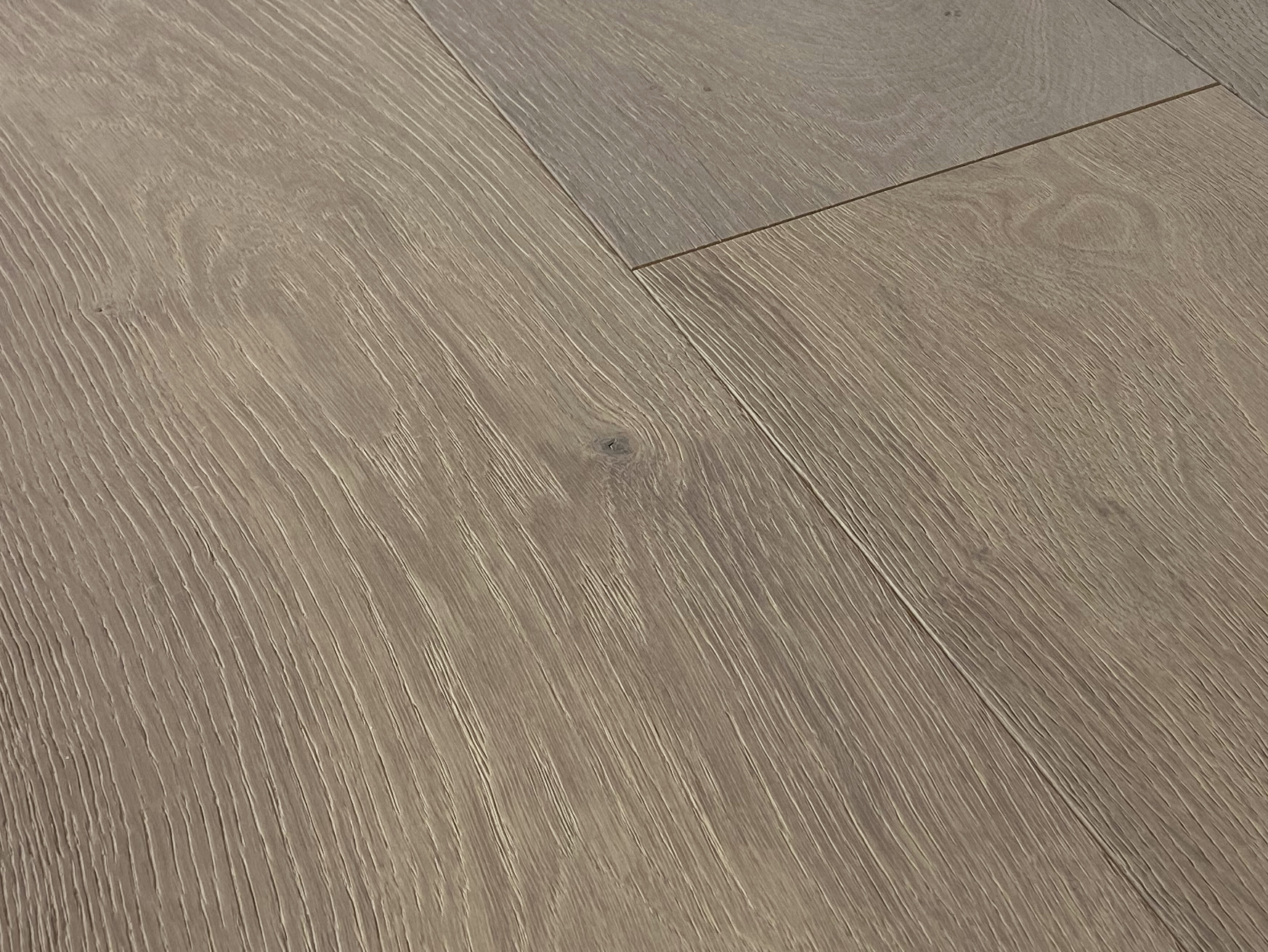 Angled close-up of a plank with a wire-brushed texture, an end joint and a warm grey-brown tone
